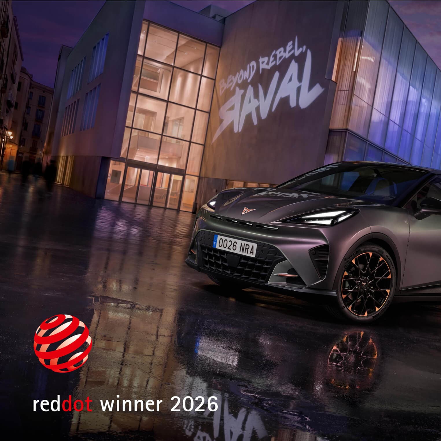 The CUPRA Raval shown in front of an urban backdrop with the phrase Beyond Rebel Raval projected onto it. In the bottom left corner is the Red Dot logo with the text Red Dot Winner 2026. 