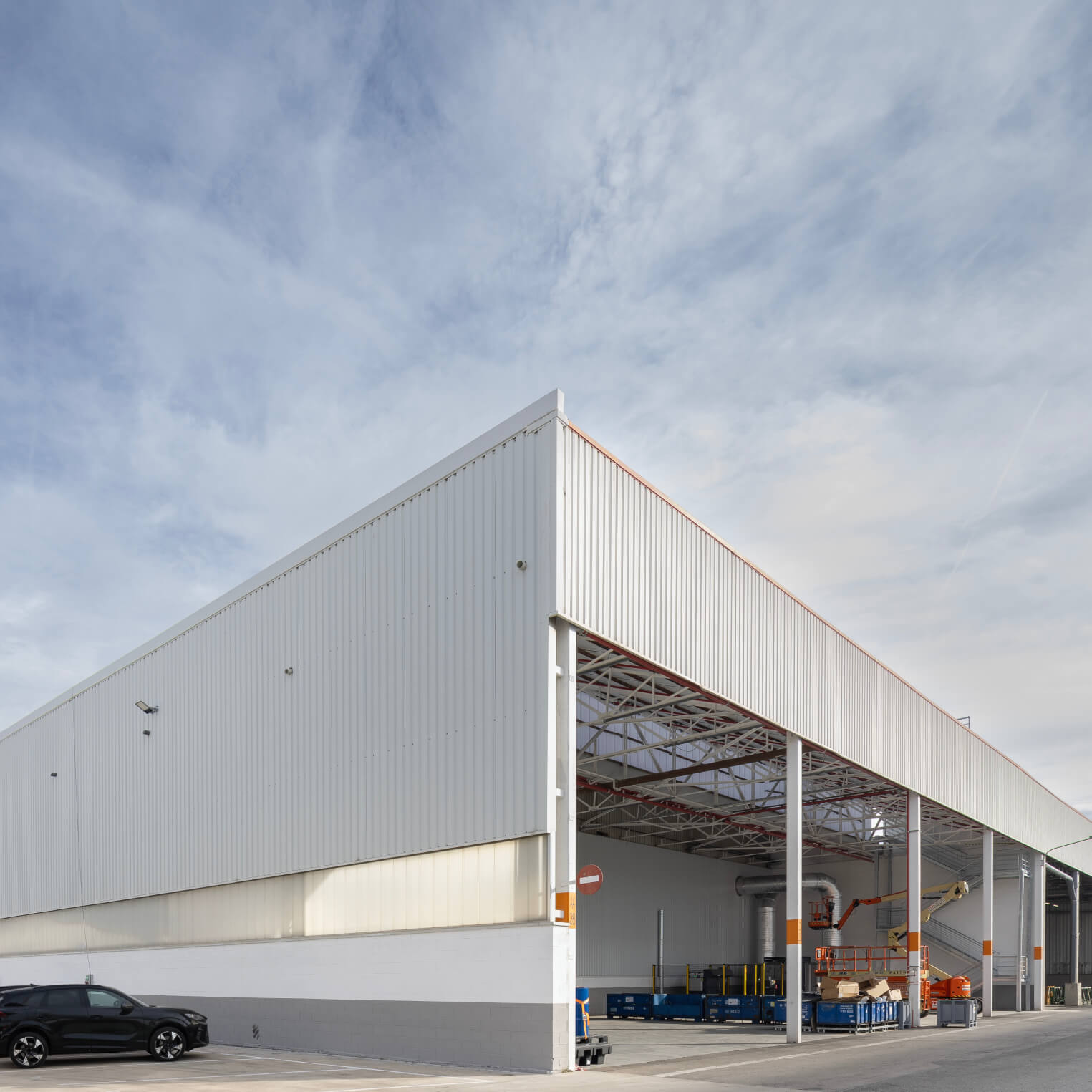 The new Circular Economy Hub in Zona Franca, Barcelona. The warehouse building is surrounded by parked cars and palm trees.