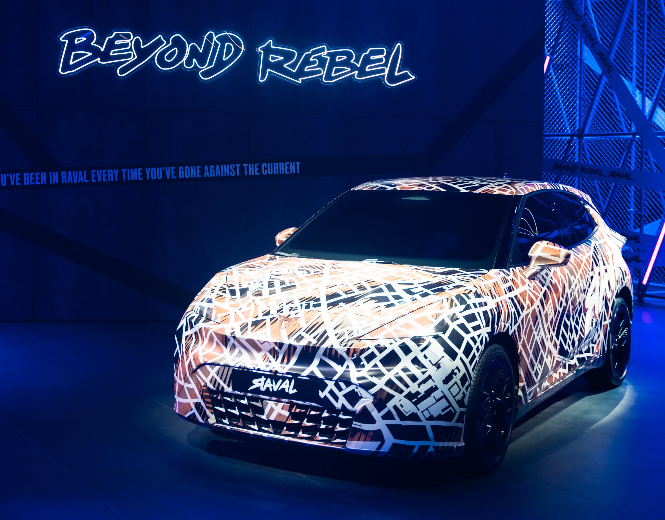 The new CUPRA Raval in camouflage wrap in front of a sign reading 'Beyond Rebel'