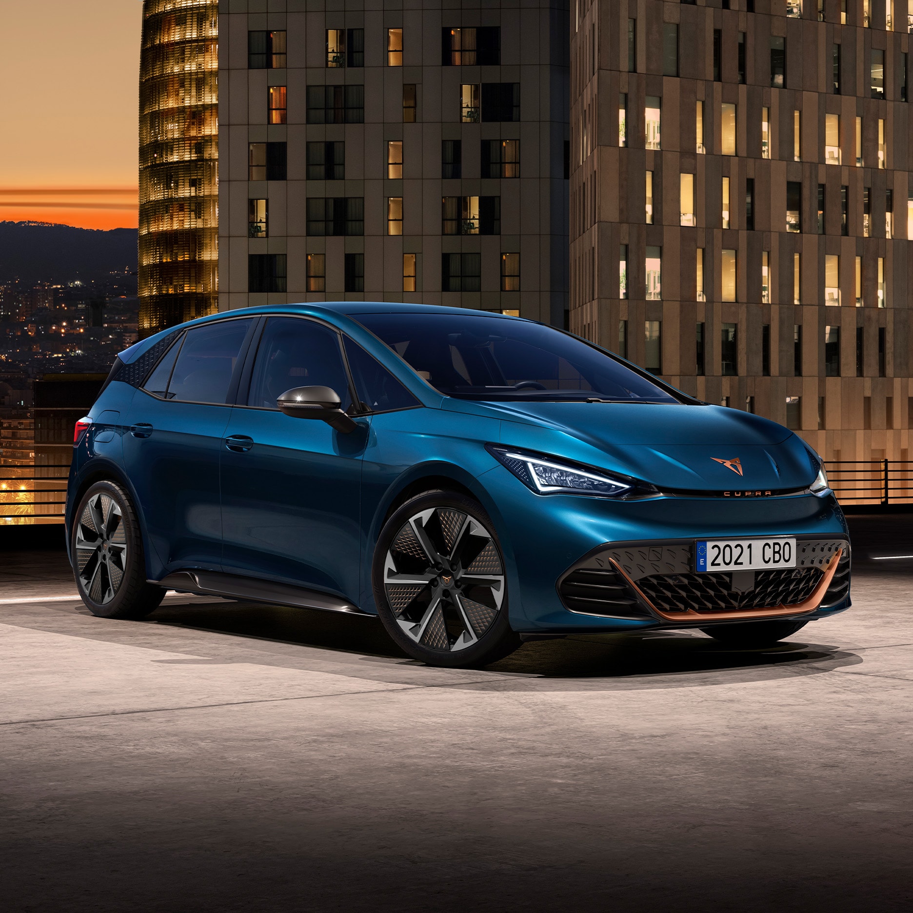A hero angle of the CUPRA Born parked outdoors at night, with different city buildings in the background.