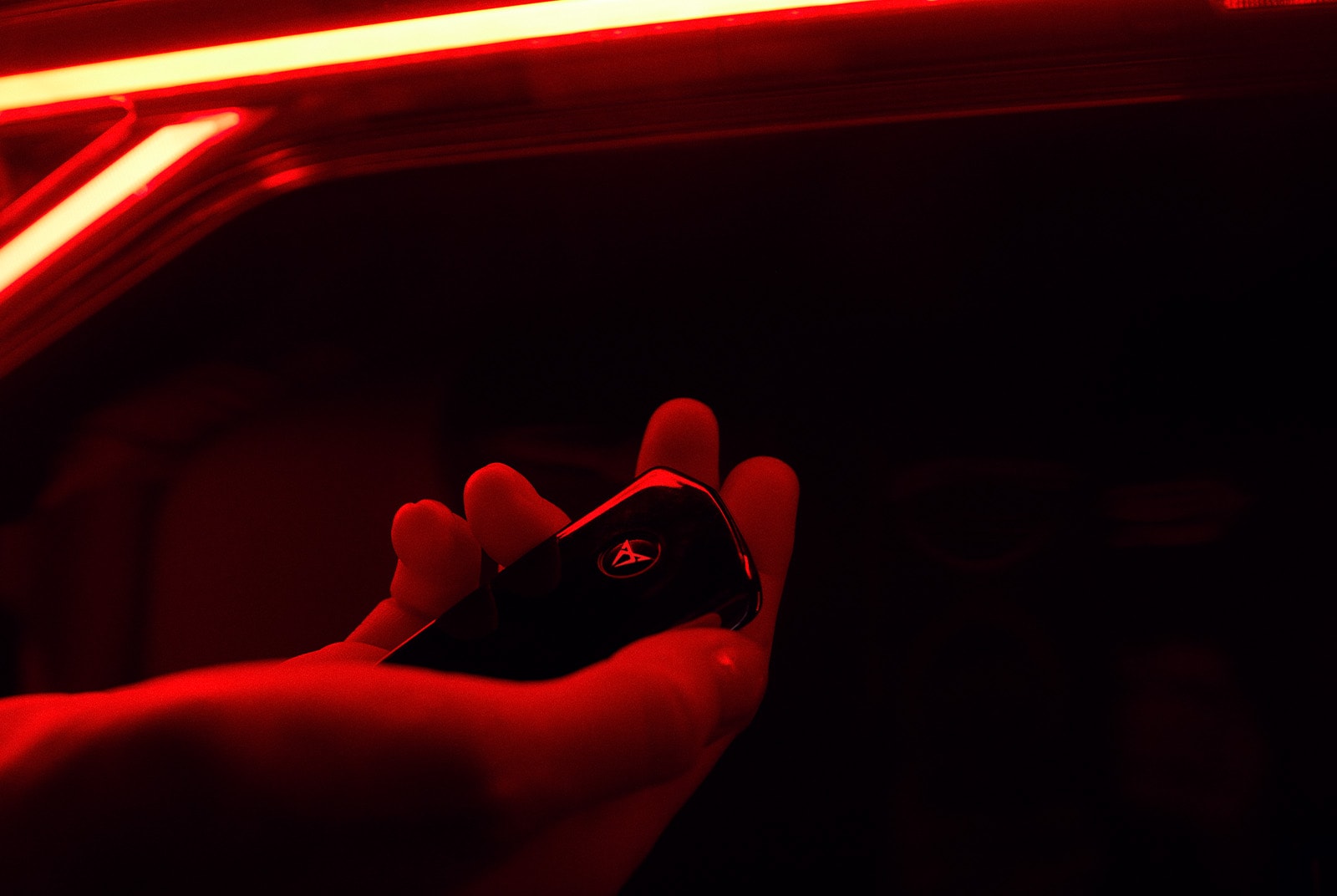Close-up of a hand holding a key of a CUPRA, with the car in the background, bathed in red light.