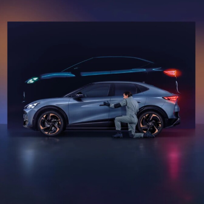 Two people standing between two parked CUPRA Terramar at twilight; a man on the right faces a woman on the left, who is standing near a dark green CUPRA Terramar and a wall-mounted charging station, while a purple Terramar is shown from the rear. 
