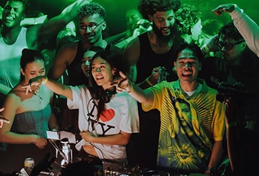 DJs playing music on their decks with a crowd of people dancing behind them