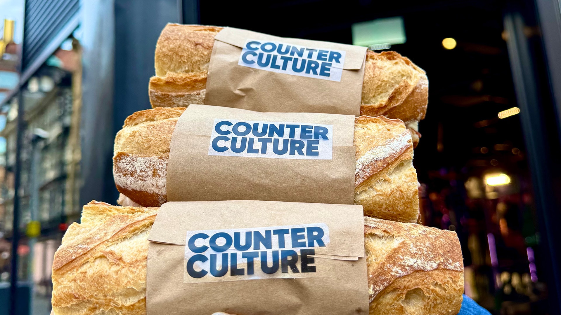 A hand holding 3 Counter Culture baguettes outside of Manchester's CUPRA City Garage