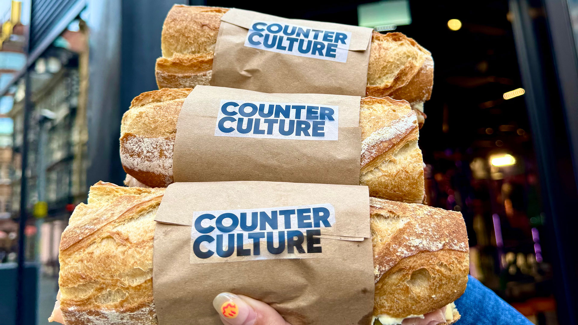 A hand holding 3 Counter Culture baguettes outside of Manchester's CUPRA City Garage