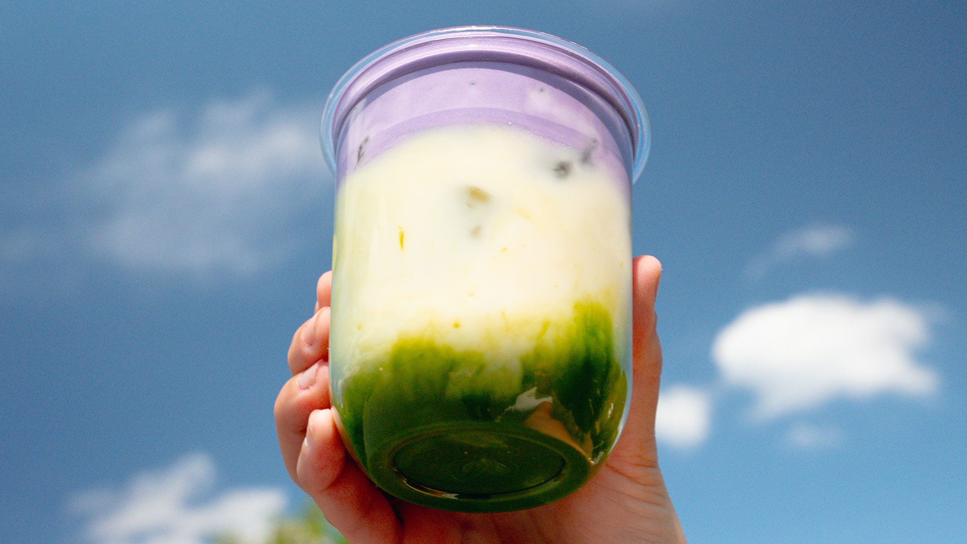 A hand holding a small jar containing white and green food
