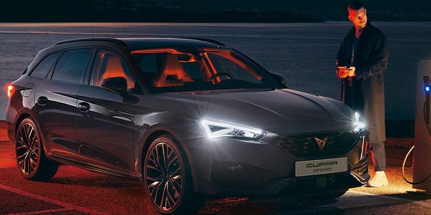 A man standing next to a CUPRA Leon while it is charging at night