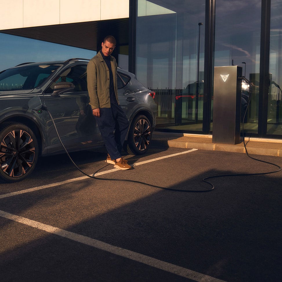 A man leaning on the side of a CUPRA Formentor e-HYBRID that's being charged