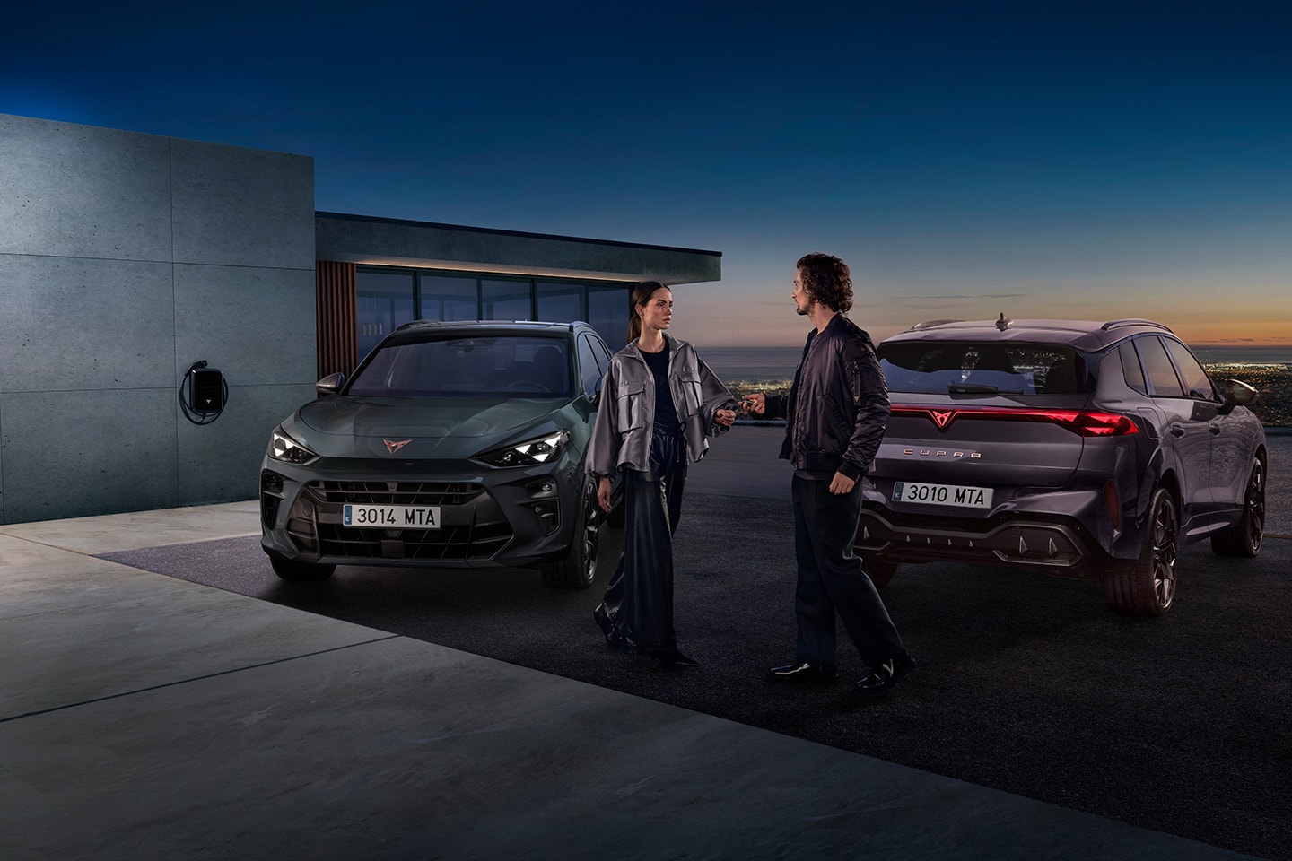 Two people standing between 2 CUPRA vehicles that are parked on a hillside location