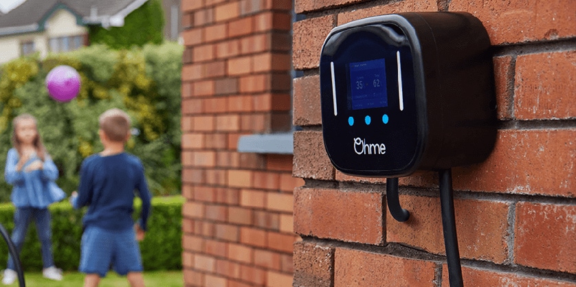 Ohme charger on brick wall with child paying in the background