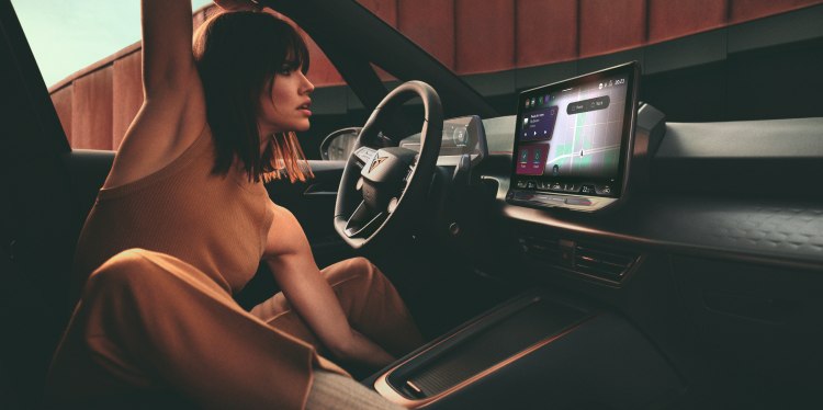A woman sitting comfortably in the driving seat of a CUPRA car and looking at the infotainment screen