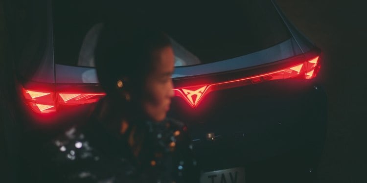 Rear view of an electric CUPRA car at night with the taillights illuminated and a person walking away from the car