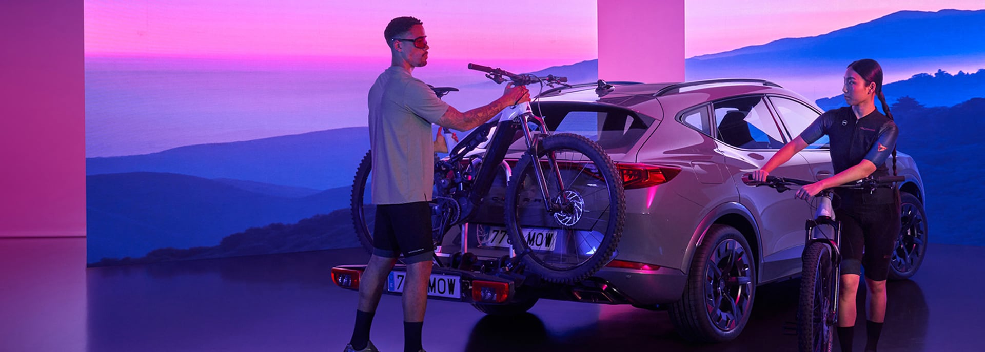 A man and woman standing next to a CUPRA. The woman is holding a bicycle and the man is taking another bicycle from the rack on the back of the CUPRA