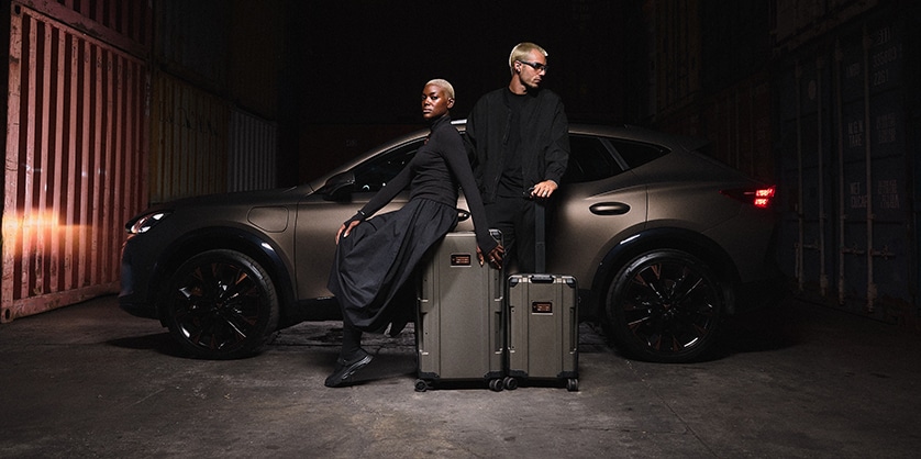 A man and woman leaning against a CUPRA in a dark room with two suitcases in front of them