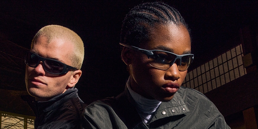 A man and woman wearing sunglasses in a dark room, looking at the camera