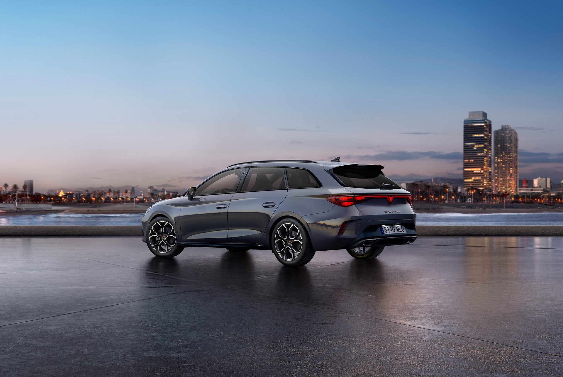 Rear view shot of new CUPRA Leon Estate glossy grey car model with dynamic chassis control, plus black and copper alloy wheels. City in the background at sunset.