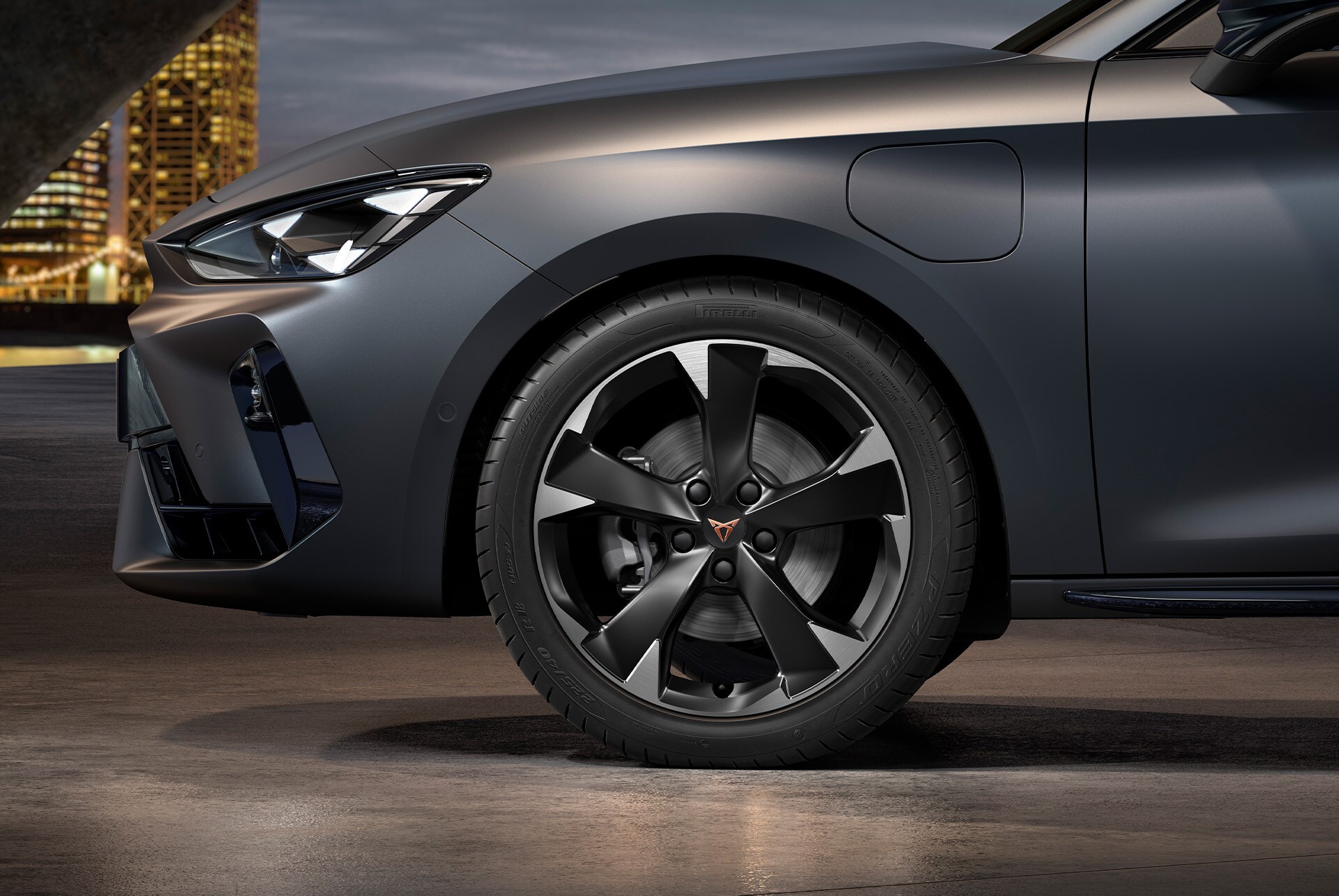 front side view of left machined silver and black Garbi alloy wheel for the CUPRA Leon Estate, tyres, signature headlights and grey body