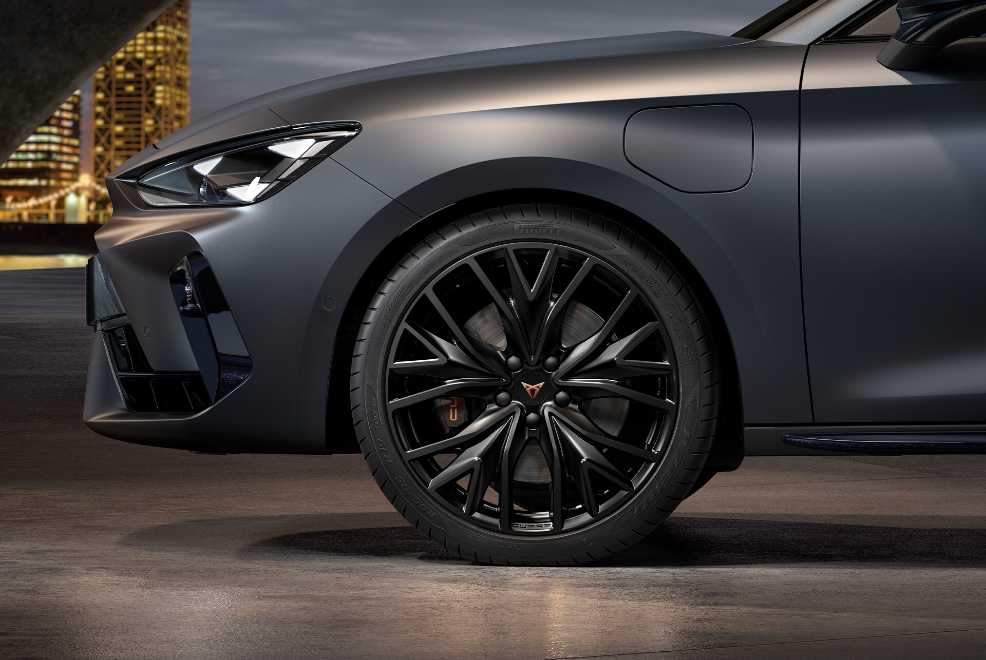 front side view of left machined alloy wheel in black and copper for the CUPRA Leon Estate, tyres, signature headlights and grey body