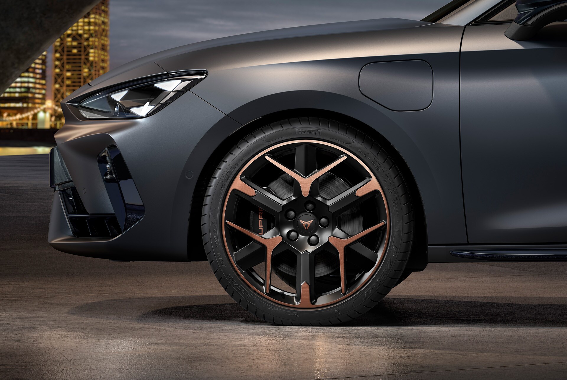 front side view of left forged alloy wheel in copper and black for the CUPRA Leon Estate, tyres, signature headlights and grey body