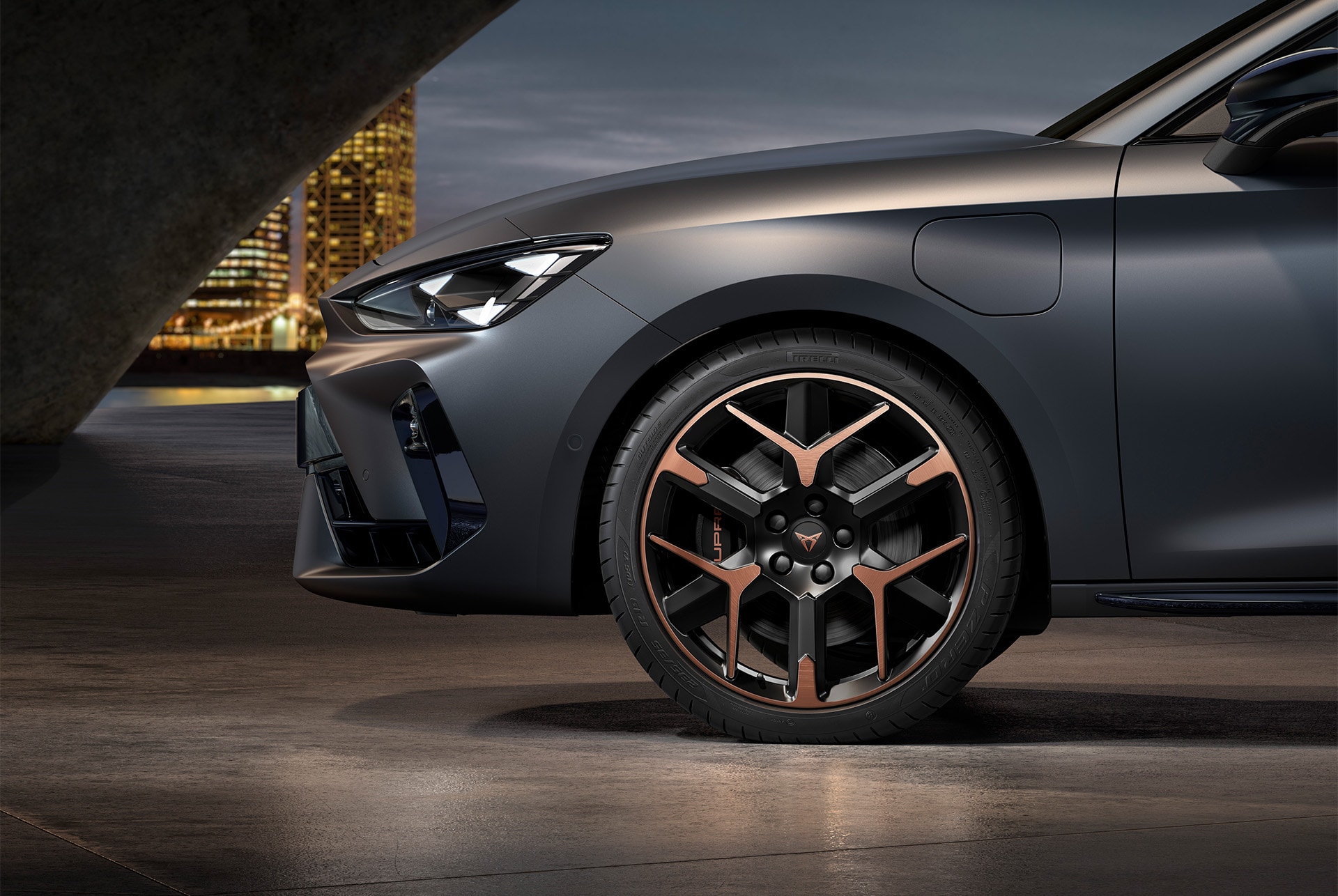 Font side view of left forged alloy wheel in copper and black for the CUPRA Leon, tyres, signature headlights and matt grey body
