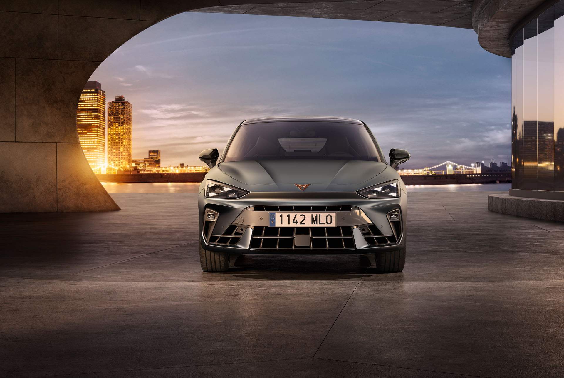 front view of a olive CUPRA Leon with the city lights shining in the background