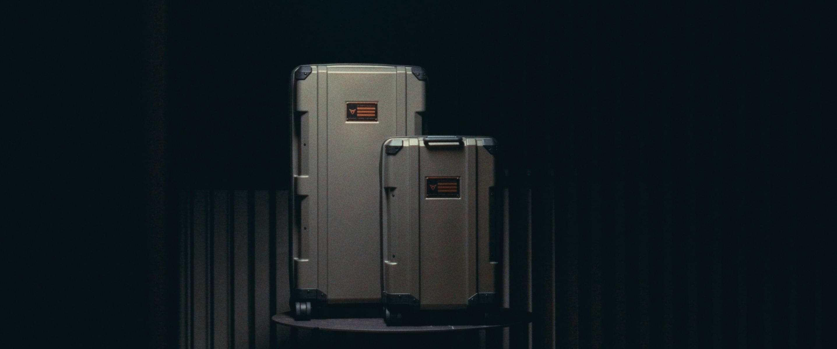 Two hard-shell suitcases of varying sizes are displayed in a room with a black background.