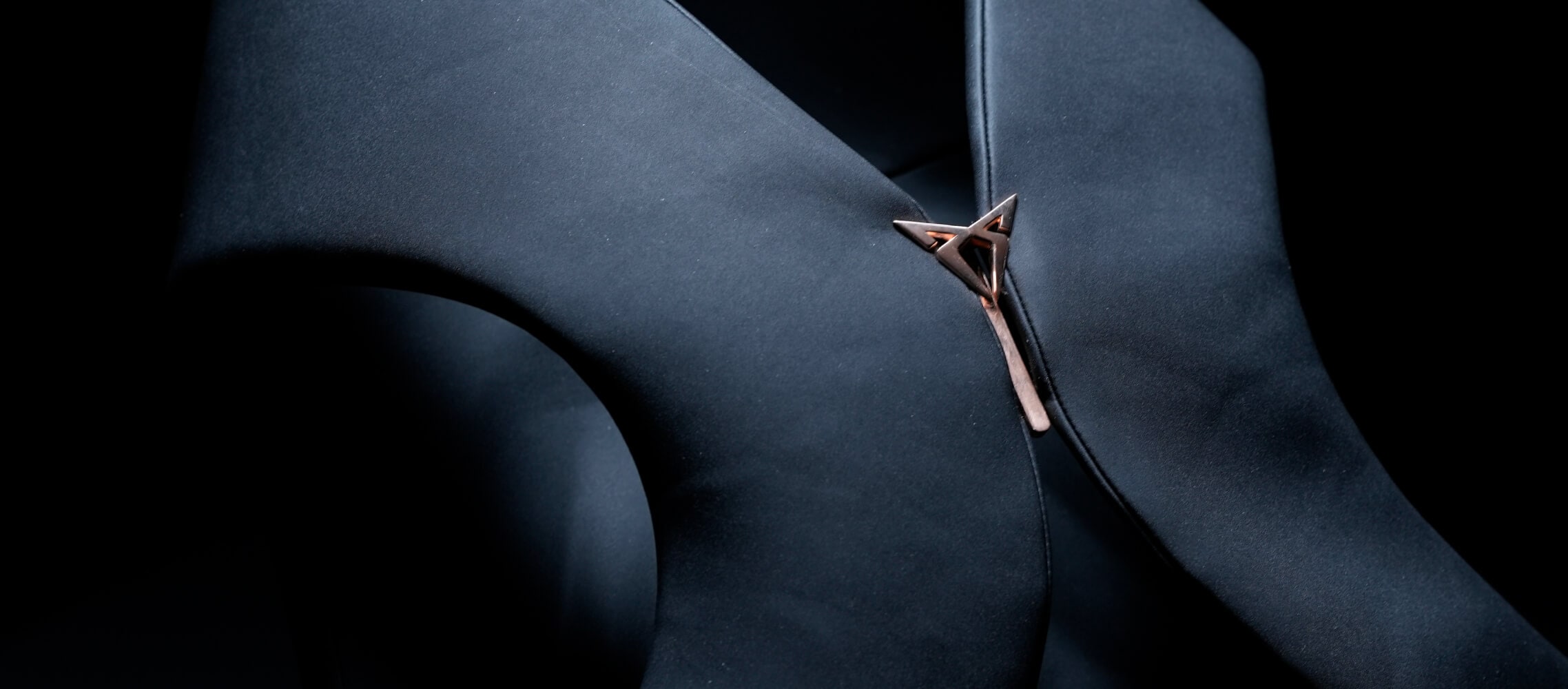 A close-up shot of dark fabric garment with a unique metal fastener, against a dark background. A close-up shot of dark fabric garment with a unique metal fastener, against a dark background.