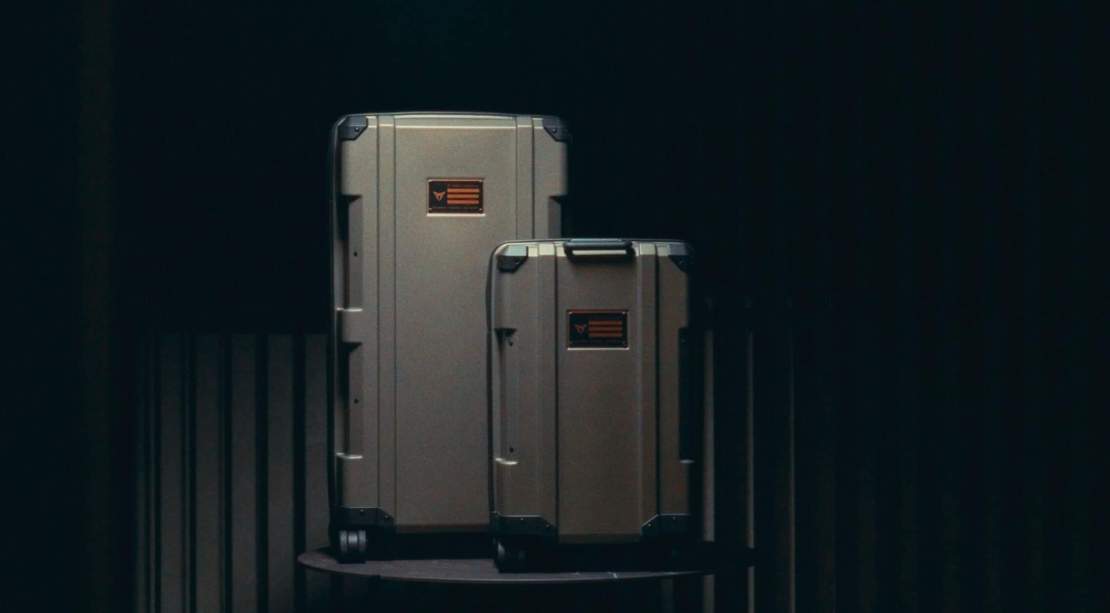 Two hard-shell suitcases of varying sizes are displayed in a room with a black background. Two hard-shell suitcases of varying sizes are displayed in a room with a black background.