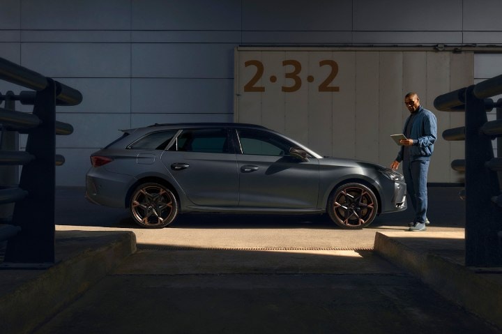 A CUPRA specialist holding a tablet whilst inspecting a CUPRA vehicle A CUPRA specialist holding a tablet whilst inspecting a CUPRA vehicle