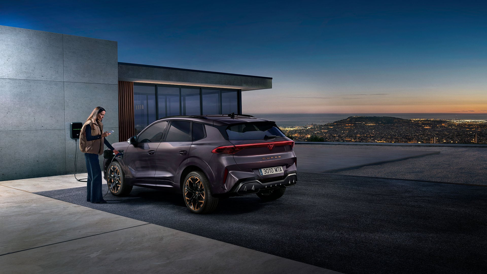 A woman using a wallbox charger to charge a purple CUPRA Tavascan