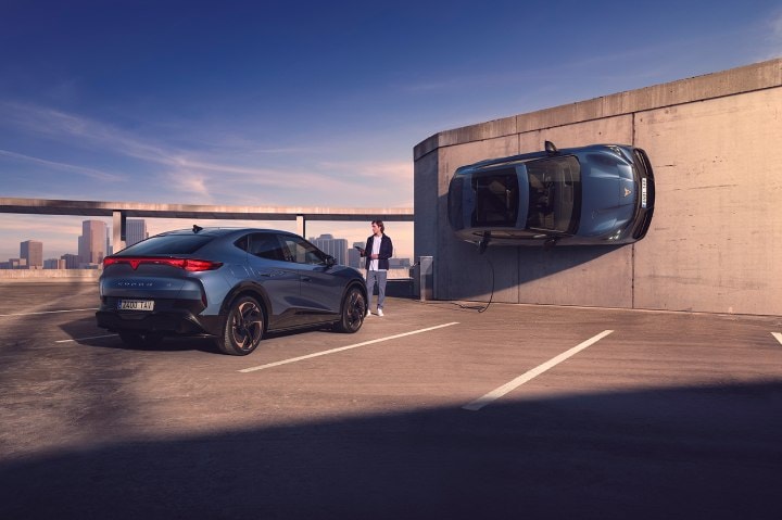 A man holding a tablet and looking at a CUPRA car whilst another CUPRA car is charging parked on the side of a wall A man holding a tablet and looking at a CUPRA car whilst another CUPRA car is charging parked on the side of a wall