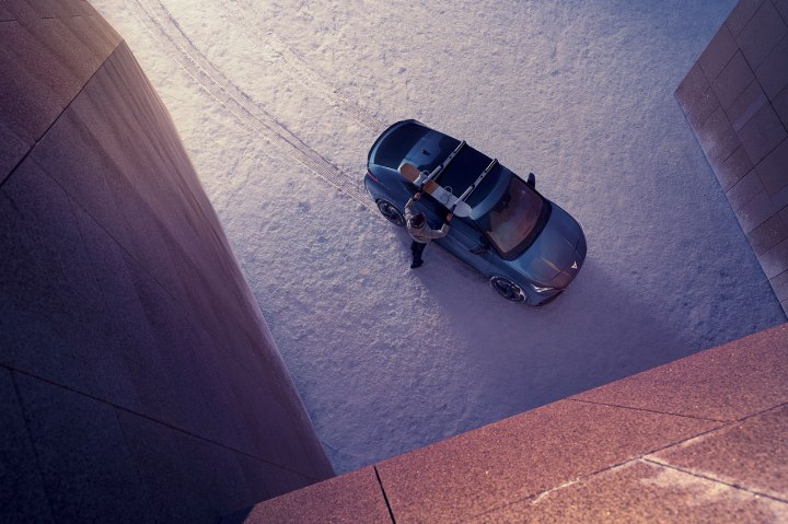 A person surrounded by snow fixing a snowboard to the roof rails on a CUPRA Tavascan A person surrounded by snow fixing a snowboard to the roof rails on a CUPRA Tavascan
