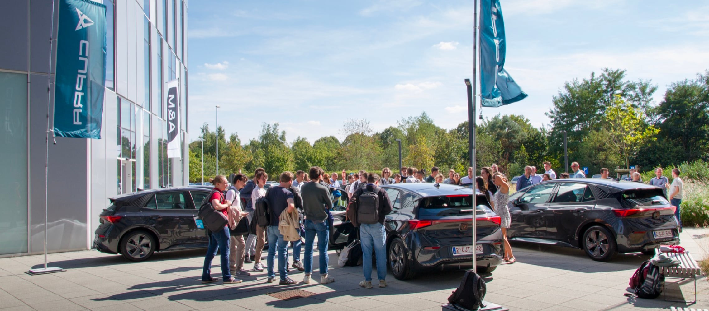 Electric vehicles, company cars outside Cegeka offices, trees and blue sky.