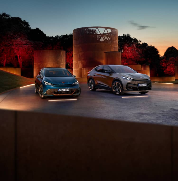 Front facing CUPRA Born and Tavascan parked outside concrete columns at night time